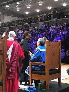 University President sitting in chair shaking hands with a student