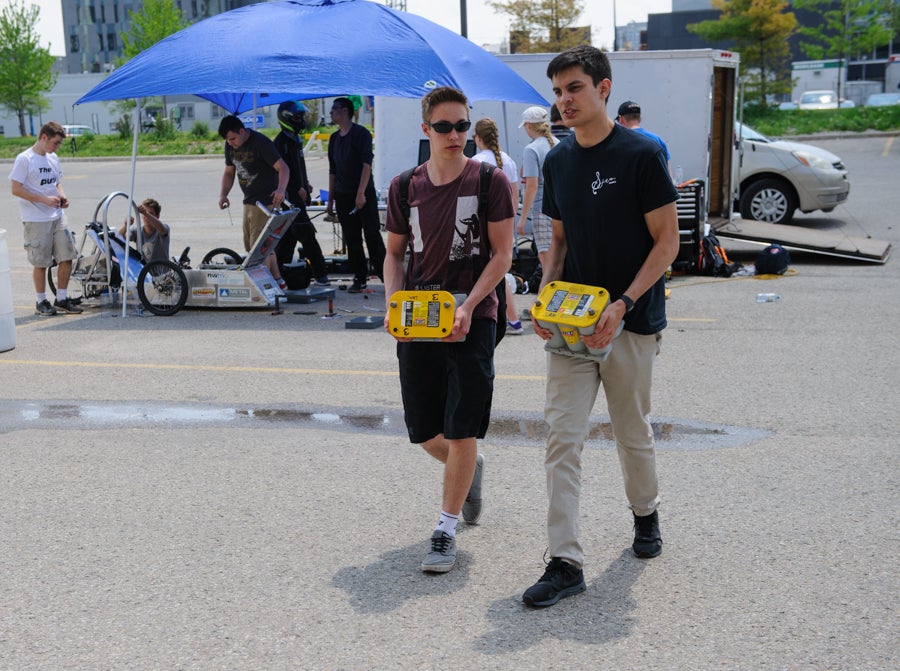 Students carry two fresh 12 V batteries to their car