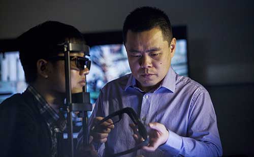 Professor Zhou Wang holding glasses with student