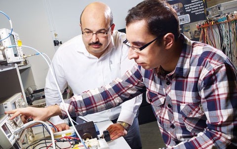 Two researchers at a laboratory bench, one pointing at an instrument display beside a power amplifier prototype