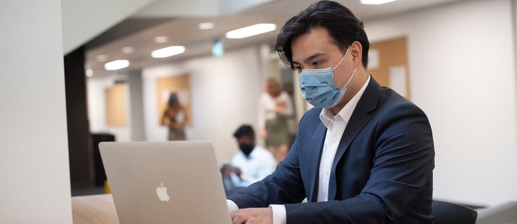 Person with a mask typing on a laptop