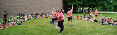 Campers sitting in a circle outside surround a small group of leaders on the inside making announcements