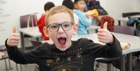 kid smiling at the camera with two thumbs up