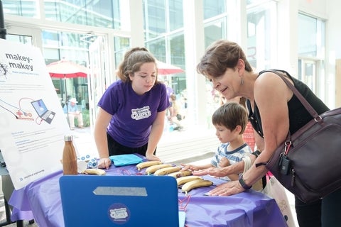 Mother and son at a table looking at a laptop screen exploring make-makey with bananas