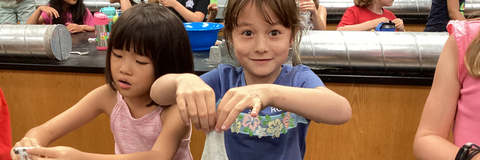 Two girl campers playing with slime in a lab setting