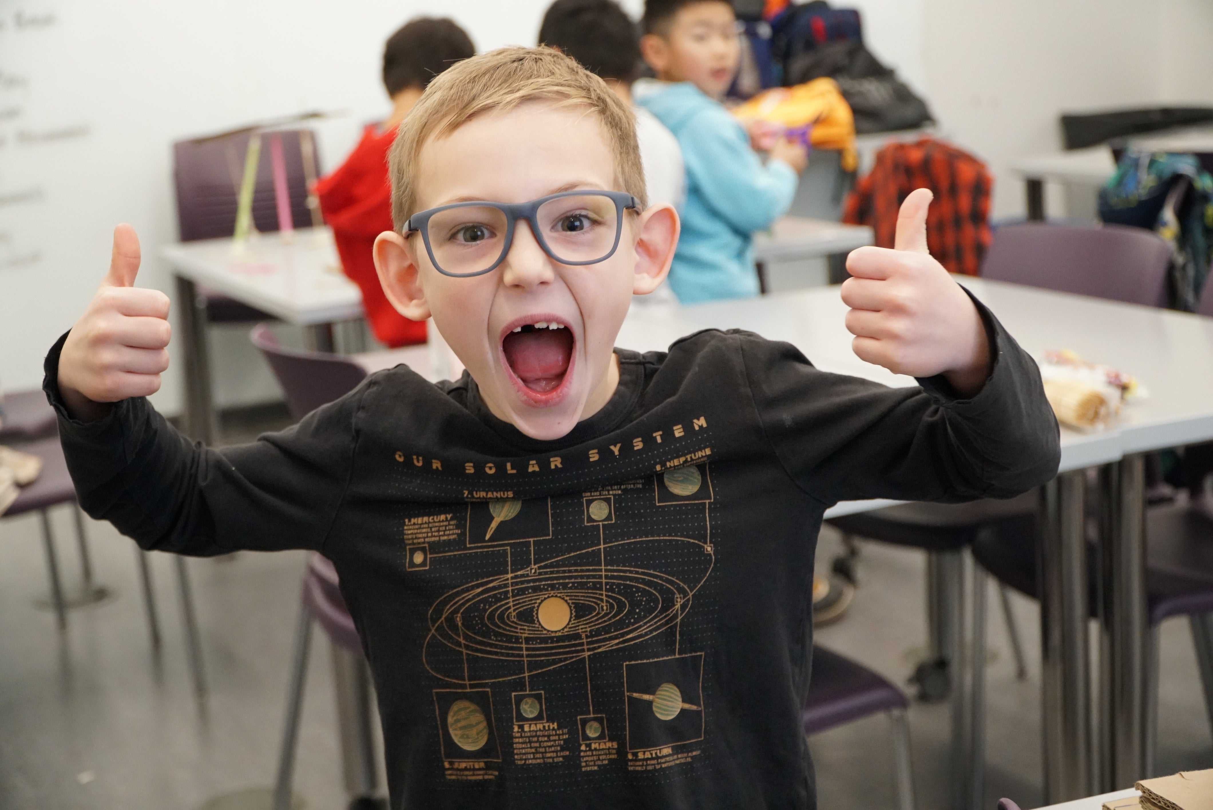 kid smiling at the camera with two thumbs up