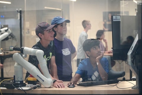 Leader and campers at a computer with a robot arm beside them