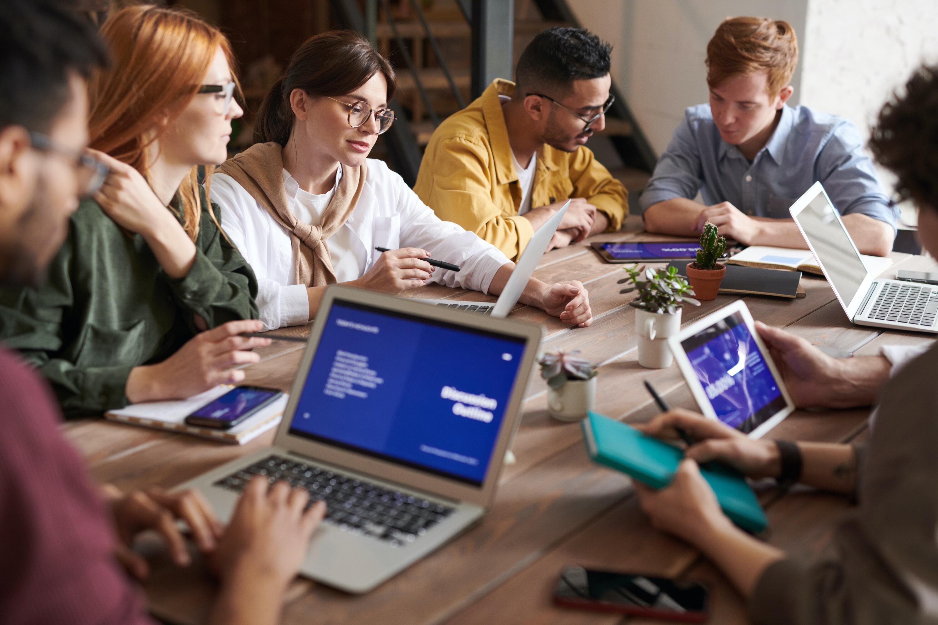 group of students sitting around a table with laptops 