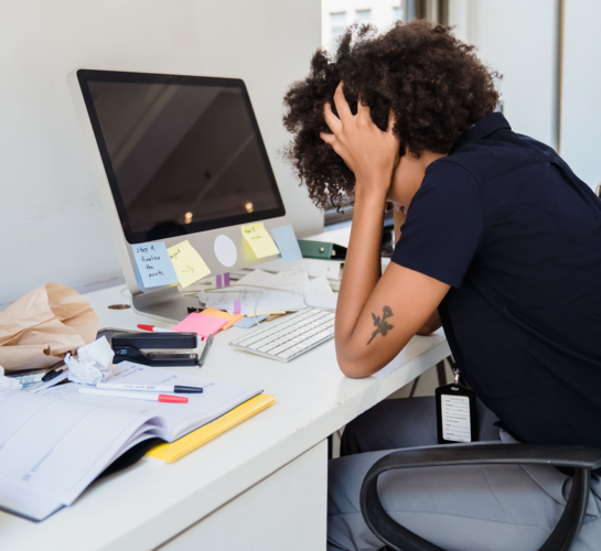 women leaning over messy desk with head in her hands.