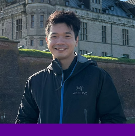 A young man stands in front of a castle, smiling.