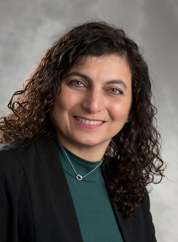 A woman with dark hair and a green shirt with a dark blazer smiles at the camera.