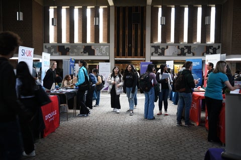 Students walking down a hallway with booths on either side.