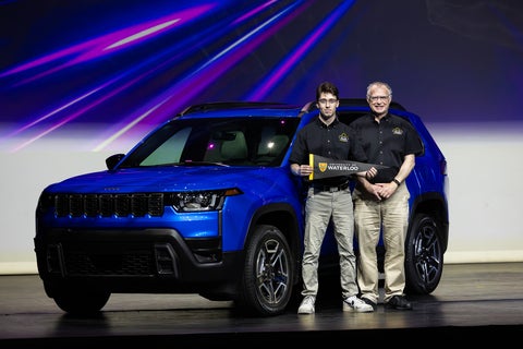 Two men pose in front of a Jeep Cherokee holding a University of Waterloo sign