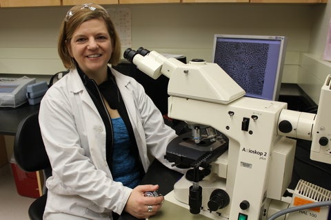 A woman sits in front of a microscope.
