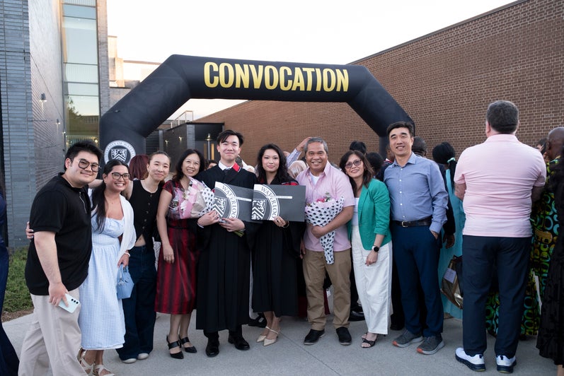 A group of new graduates and family members pose under a convocation sign