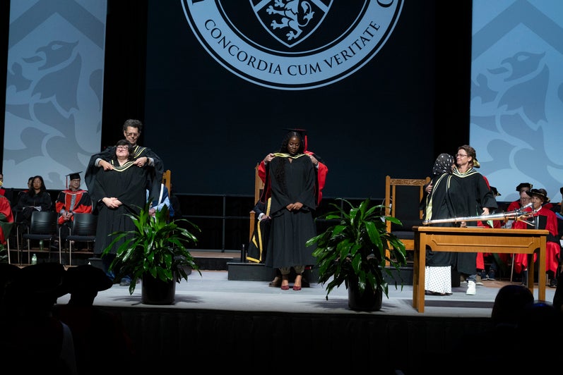 Three graduates are hooded on stage during convocation