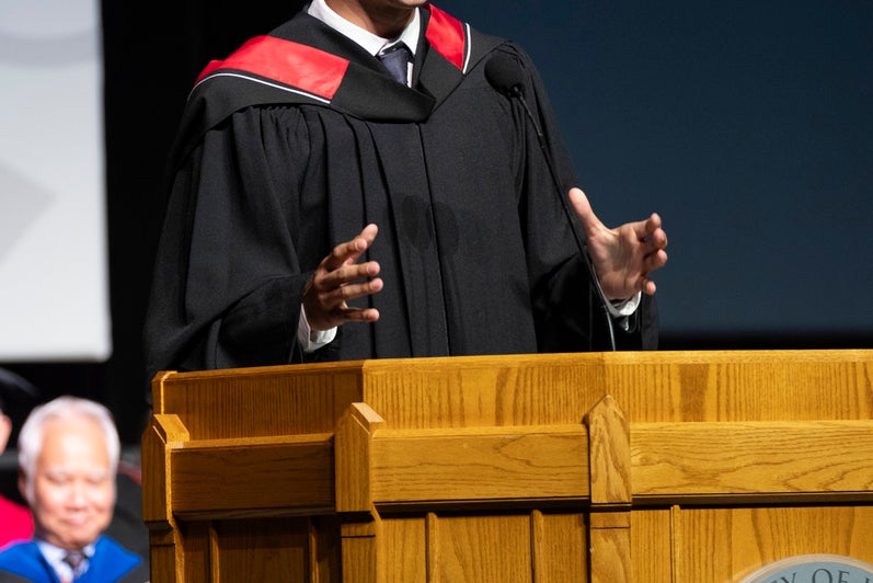 A young man delivers a speech in academic regalia at convocation