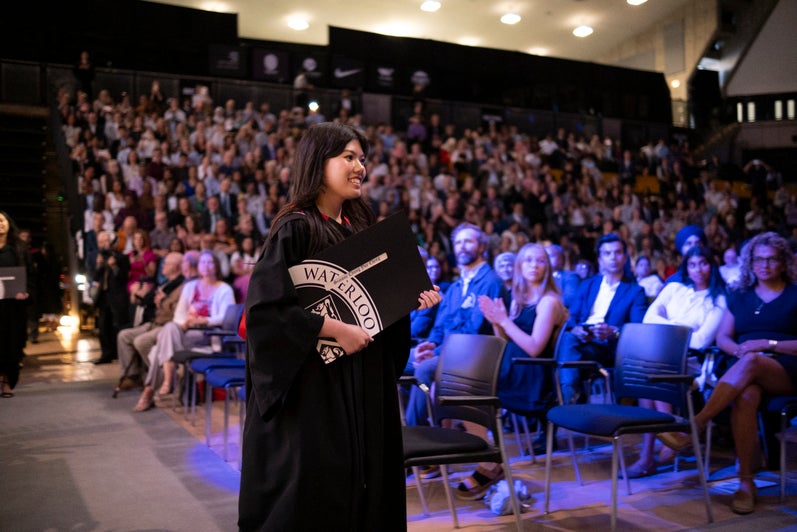 A young woman walks back to her seat holding her degree certificate at convocation