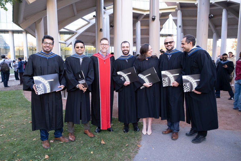 A group of men and a faculty member pose outside after convocation
