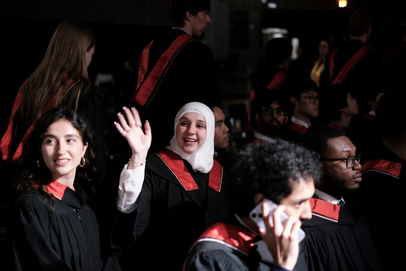 A young woman waves as she's seated for her convocation ceremony