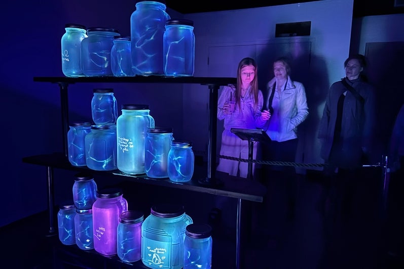 Three women look at glowing mason jars in the dark as part of an art exhibit.