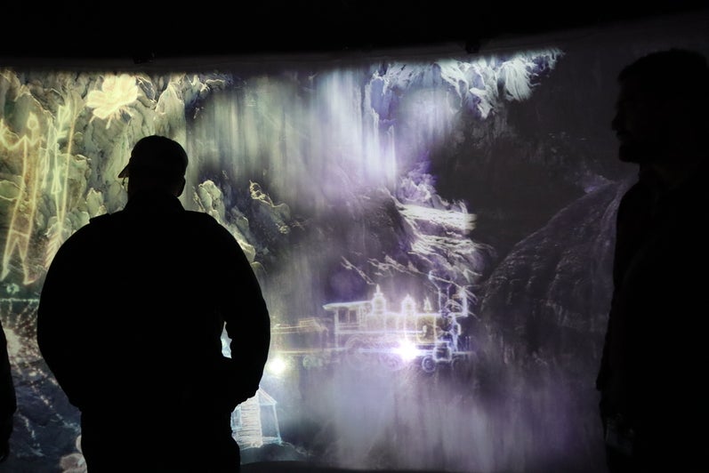 A shadow of man watches a digital screen in an art exhibit.