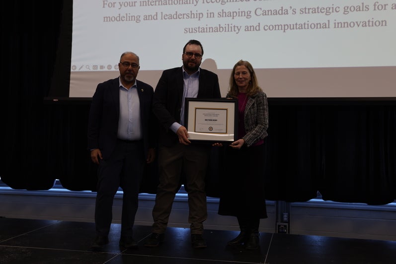 Two men and  one woman pose with a certificate on stage.
