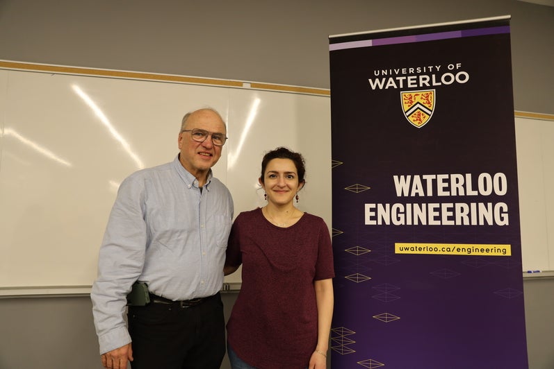A man poses with a woman beside a Waterloo Engineering sign.