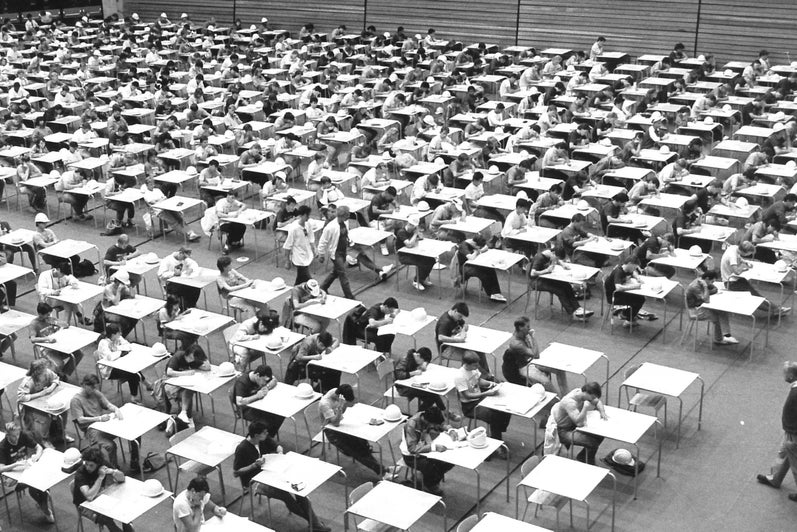 Students at exam tables in neat rows writing exams.