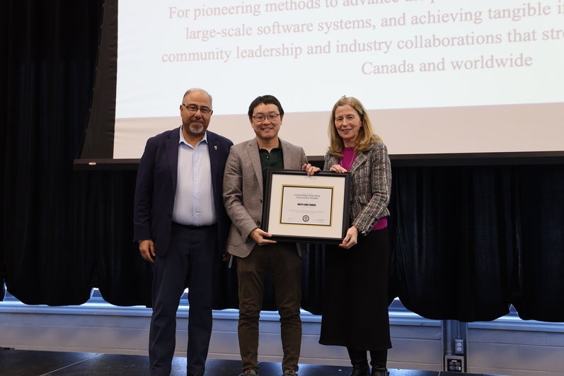 Two men and a woman pose on the stage with a certificate.