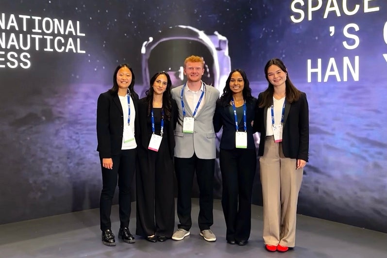 Four young women and one young man pose in front of a screen with an astronaut.