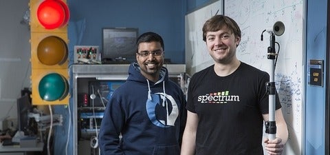 Miovision co-founders, Tony Brijpaul and Kevin Madill, standing next to a traffic light and other equipment in their office