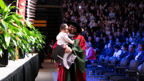 A man holds his daughter and degree after he leaves the stage