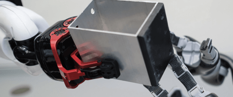 One robotic hand passing a block of metal to another robotic hand