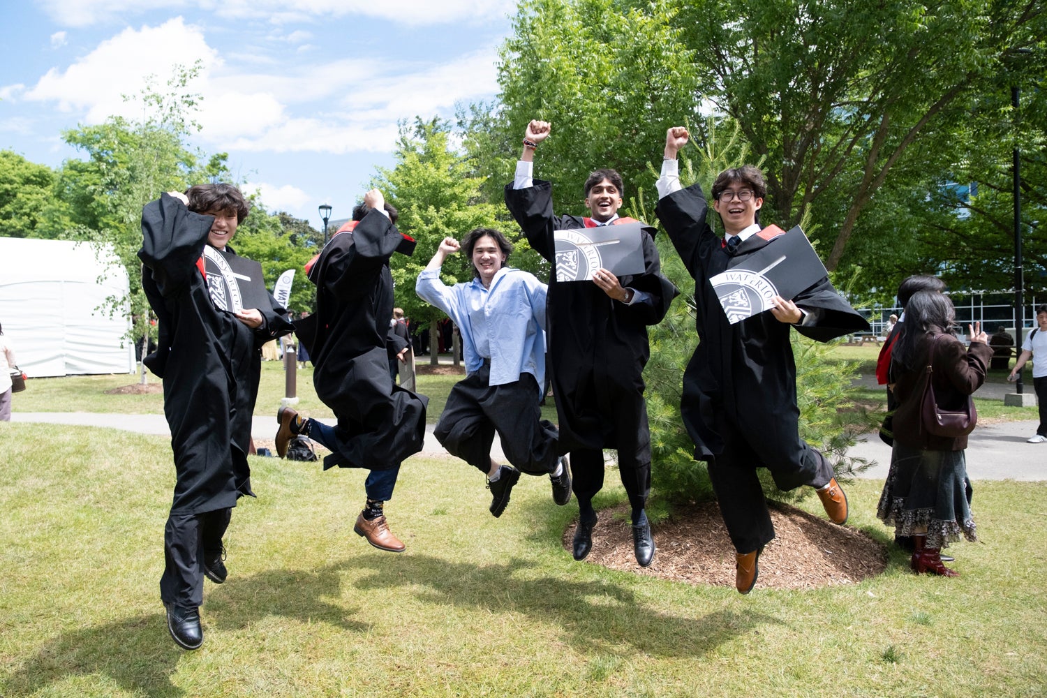 A group of graduates jump in the air while holding their degree certificates after convocation