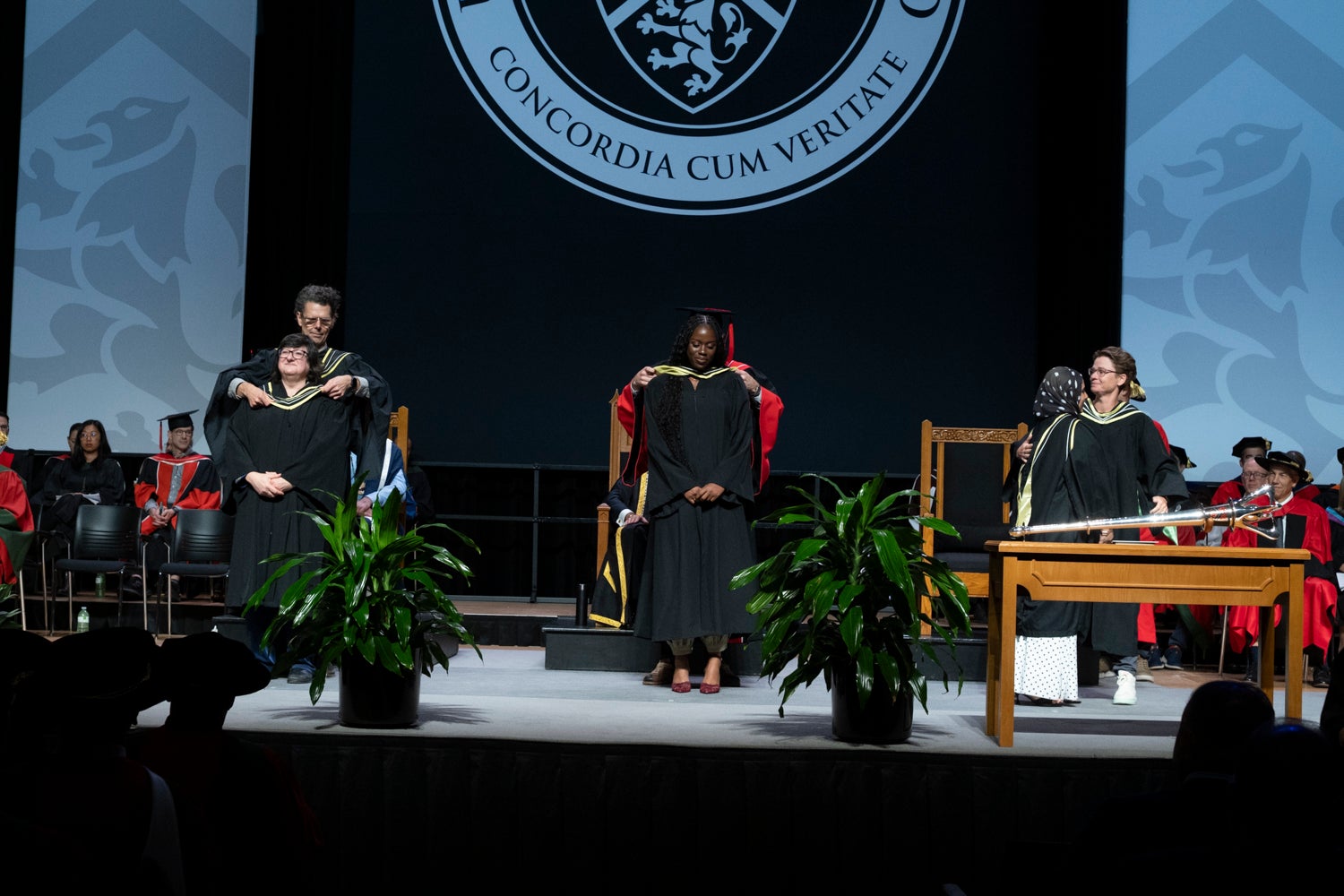 Three graduates are hooded on stage during convocation