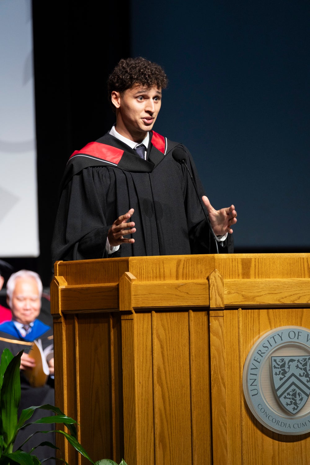 A young man delivers a speech in academic regalia at convocation