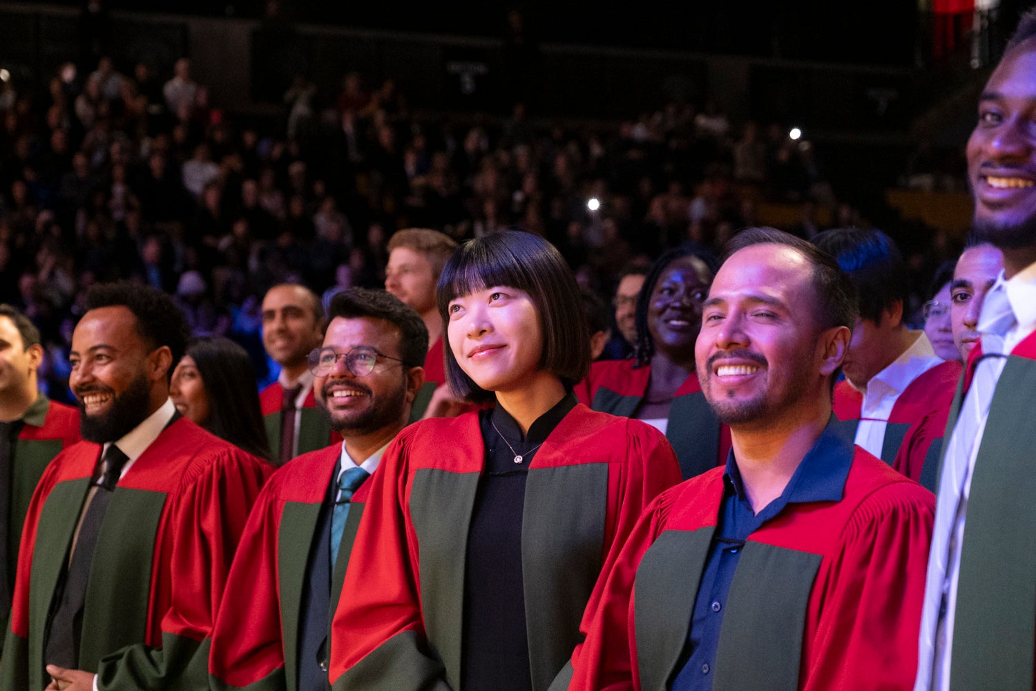 A row of gowned PhD students smile at the stage