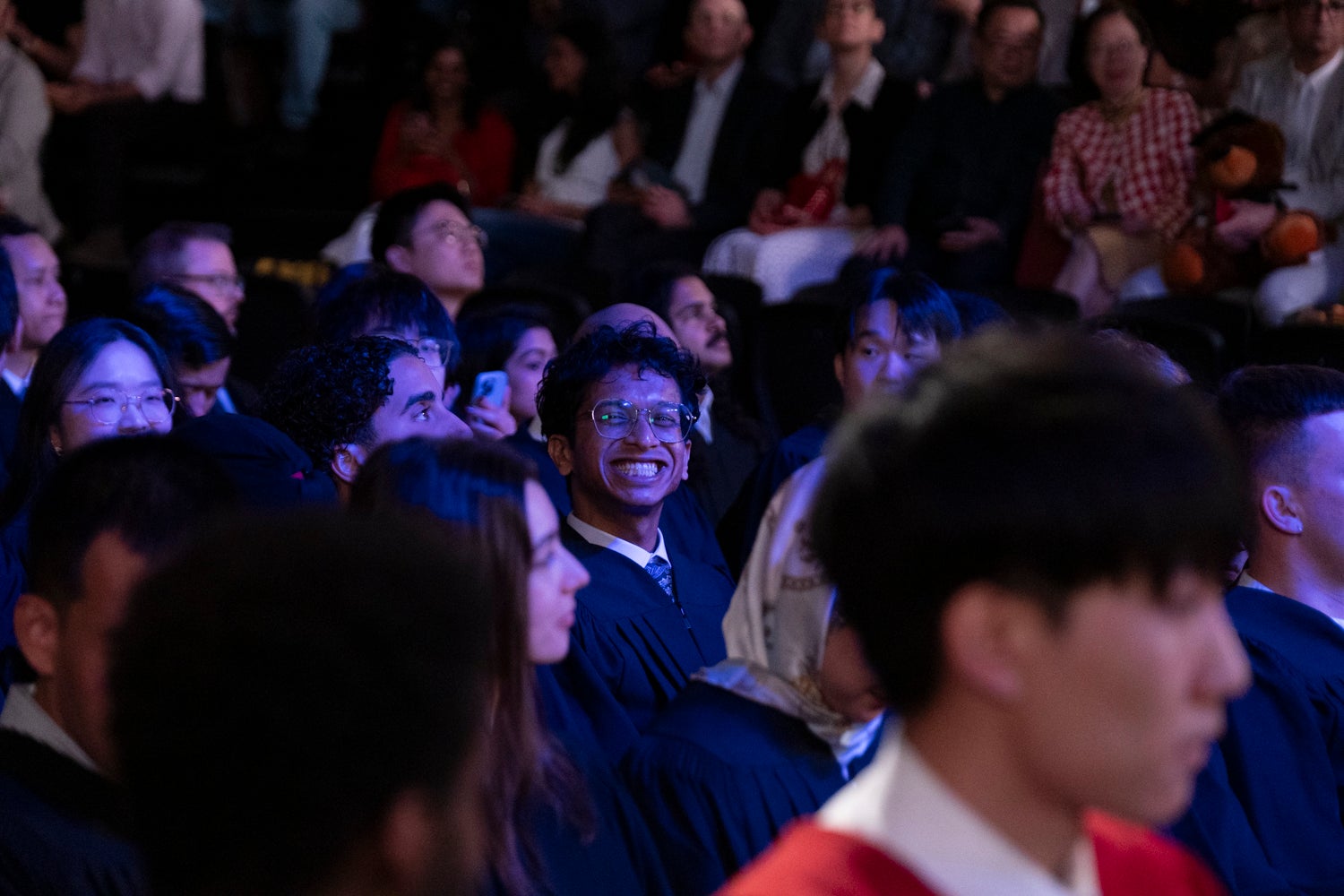 A young man smiles at the camera in the midst of the crowd at convocation