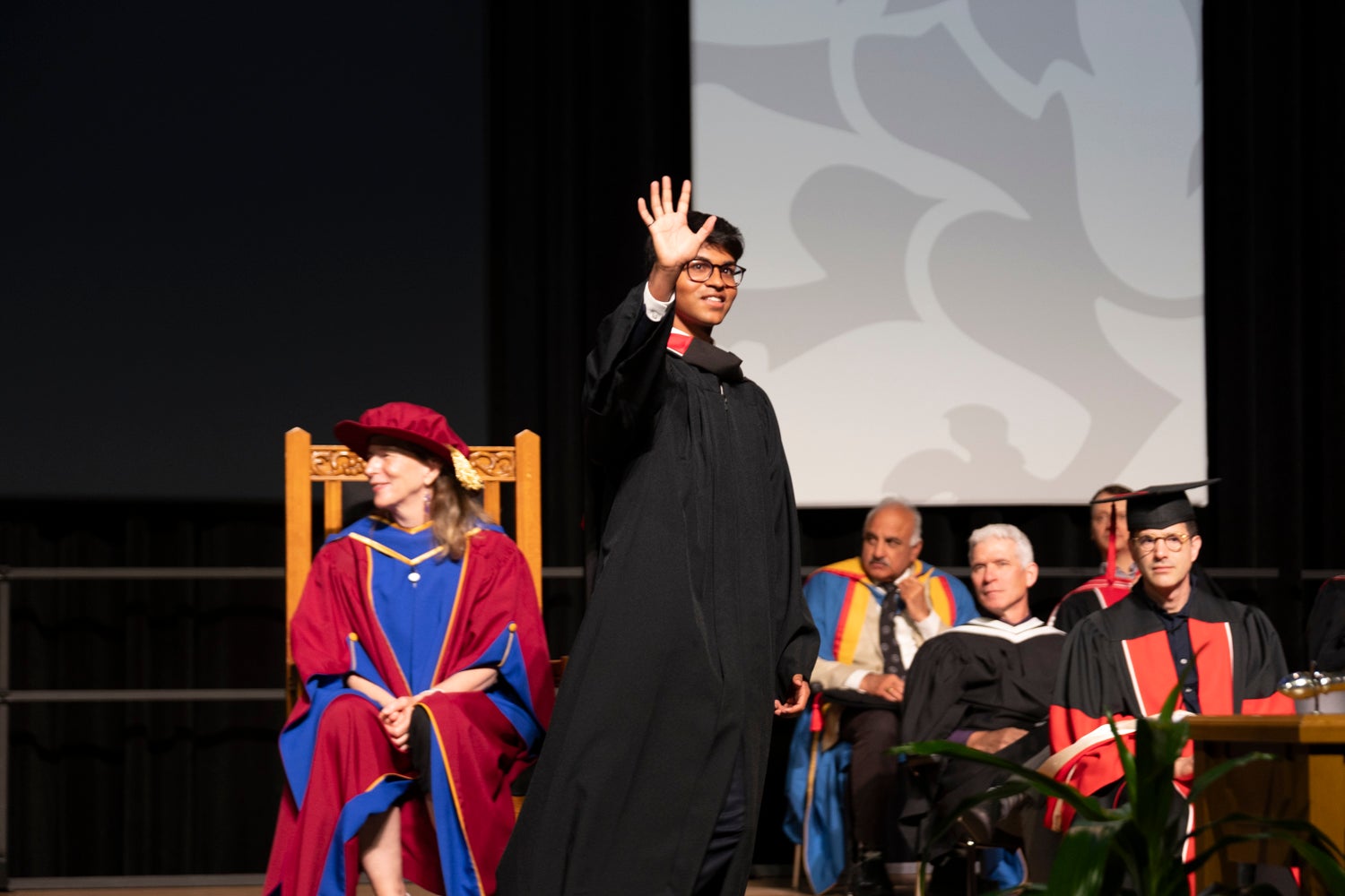 A young man crosses the stage at convocation, wearing academic regalia