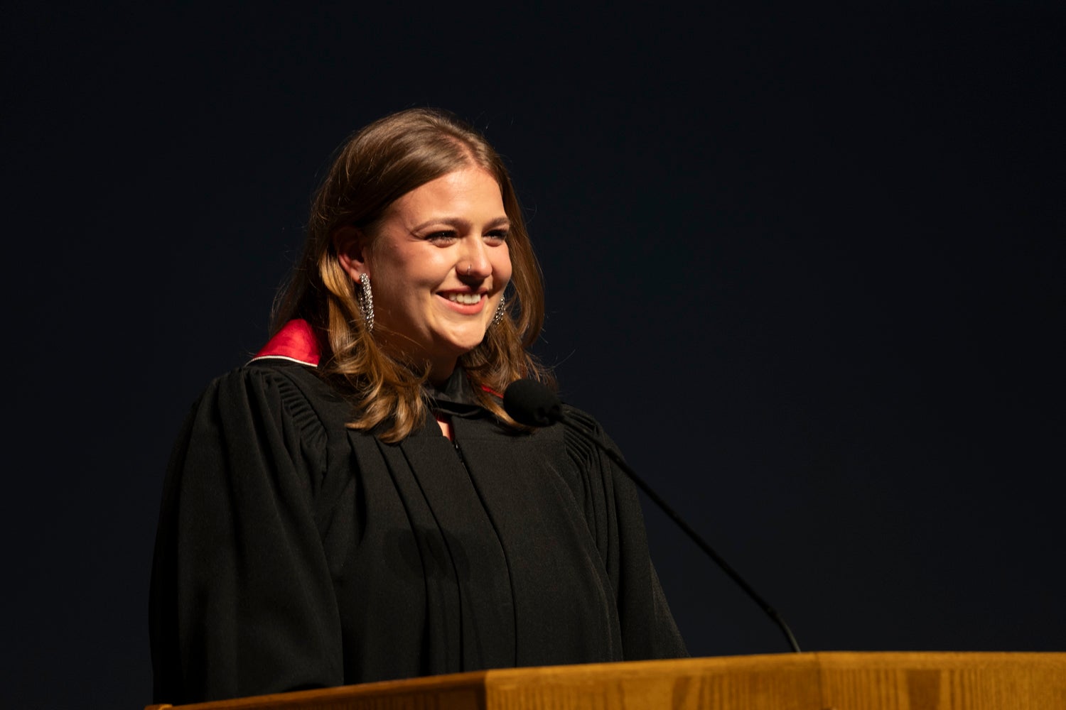 A young woman wearing academic regalia delivers a speech at the podium
