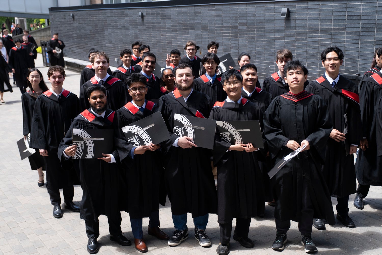 A group of newly minted graduates pose outside with the degree certificates after convocation
