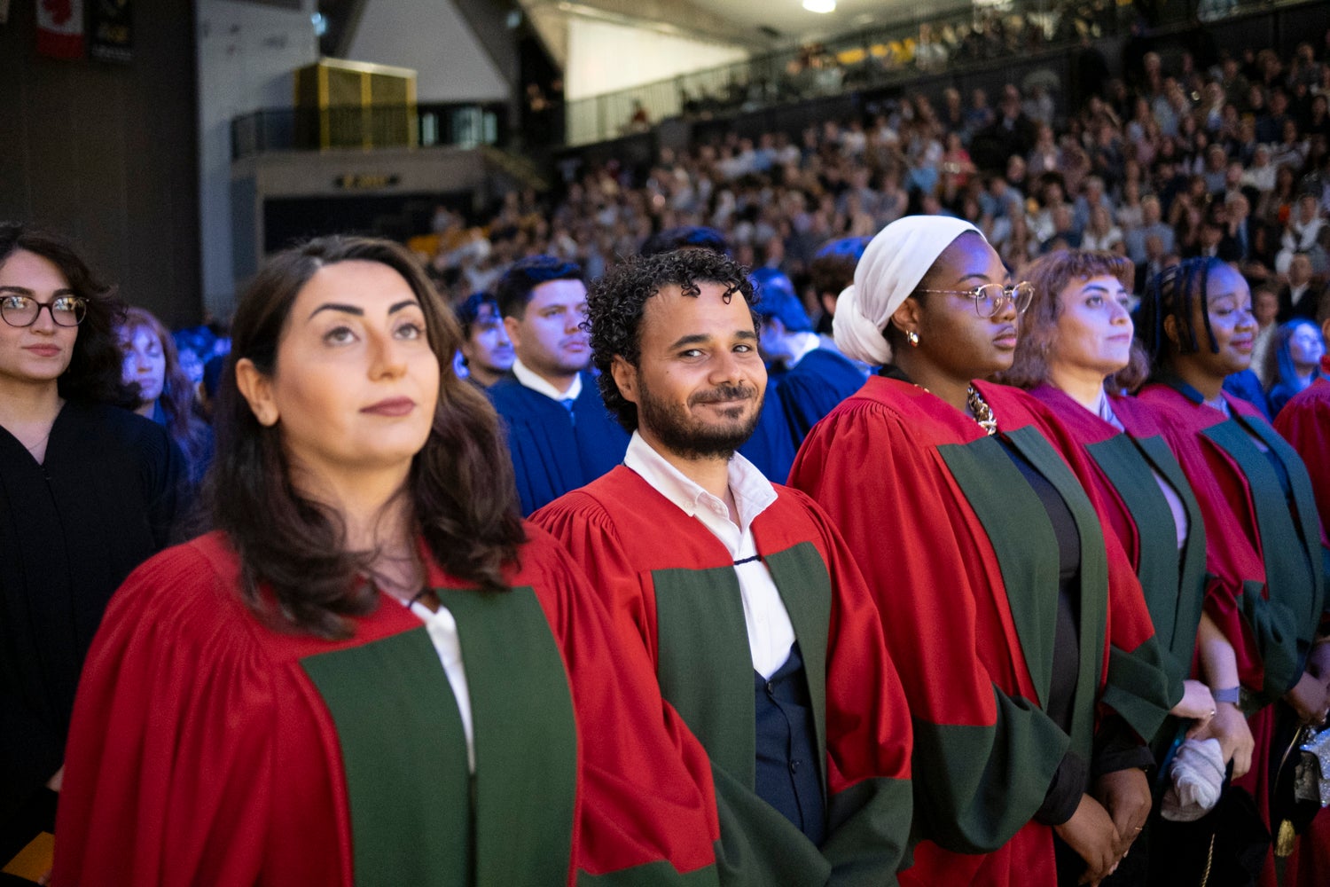 A group of PhD graduates in academic regalia stand during convocation; one young man smiles at the camera