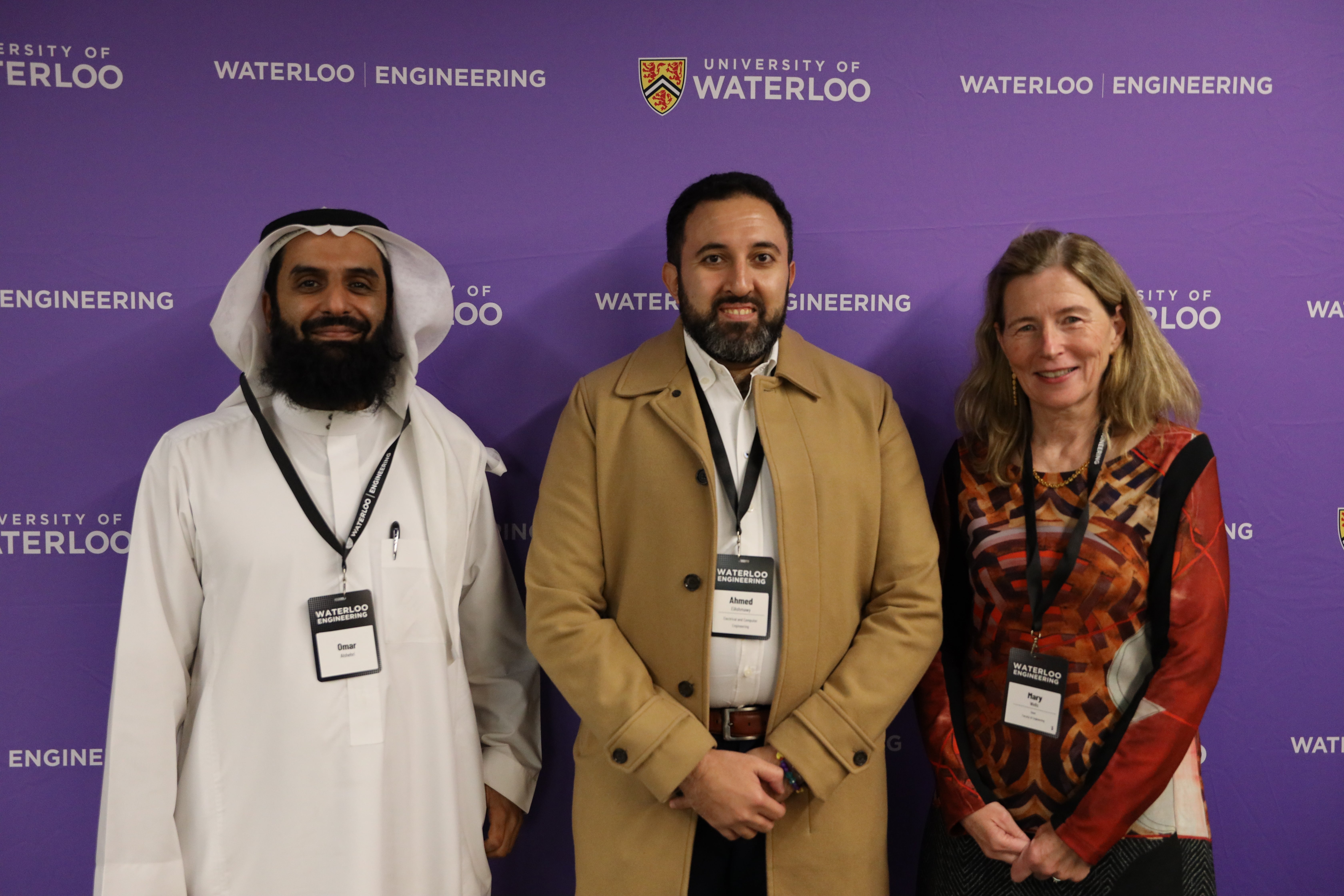 Three people stand together in front of a purple screen branded Waterloo Engineering