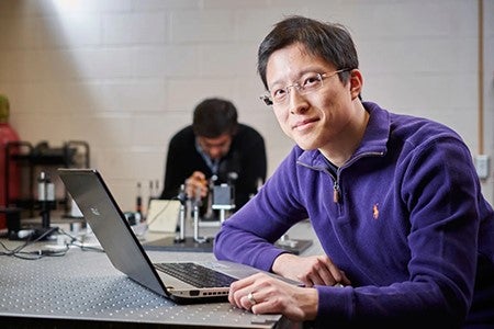 Dr. Alexander Wong sitting at laptop computer and smiling at camera