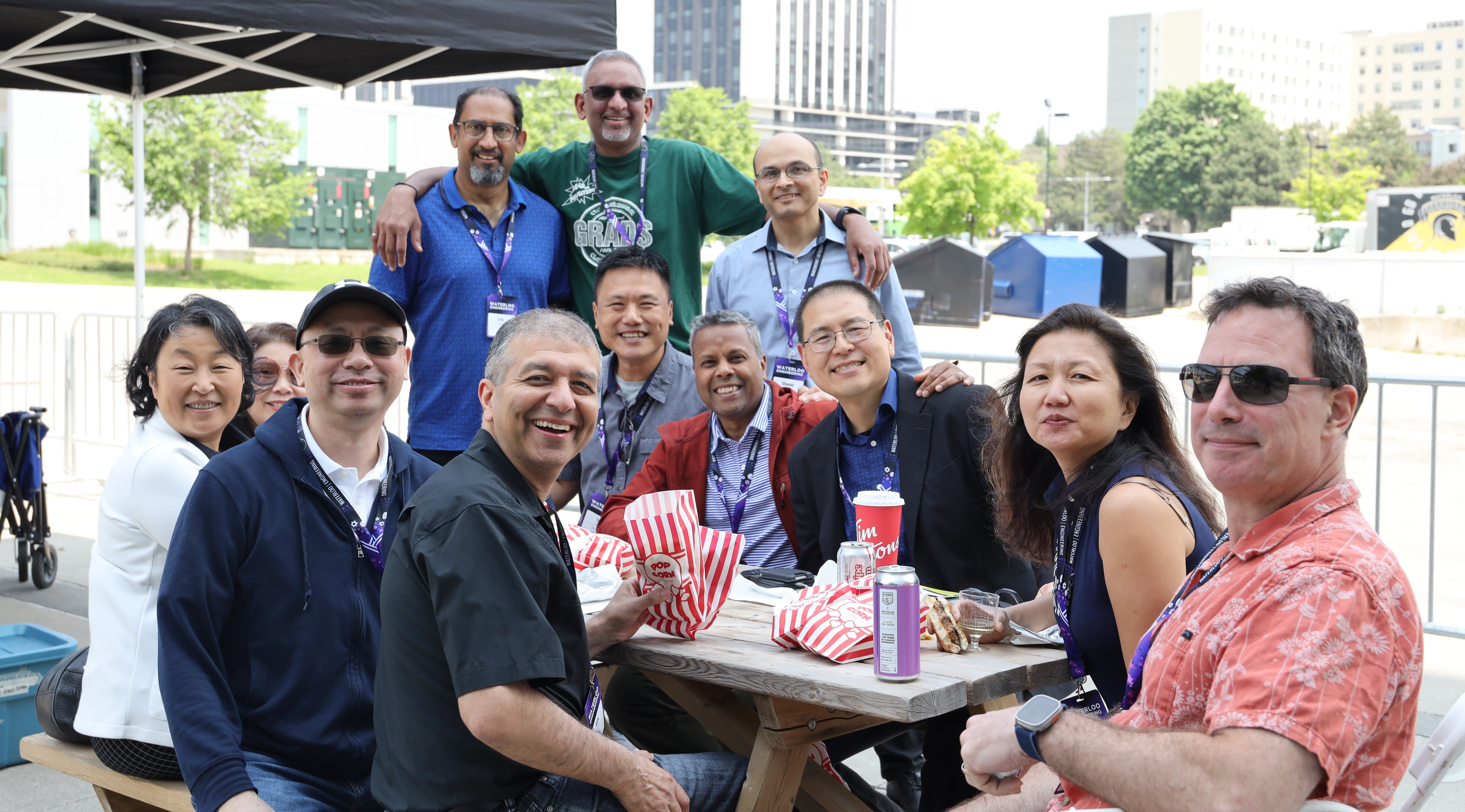 A group of engineering alumni enjoying a BBQ outside sitting at a picnic table