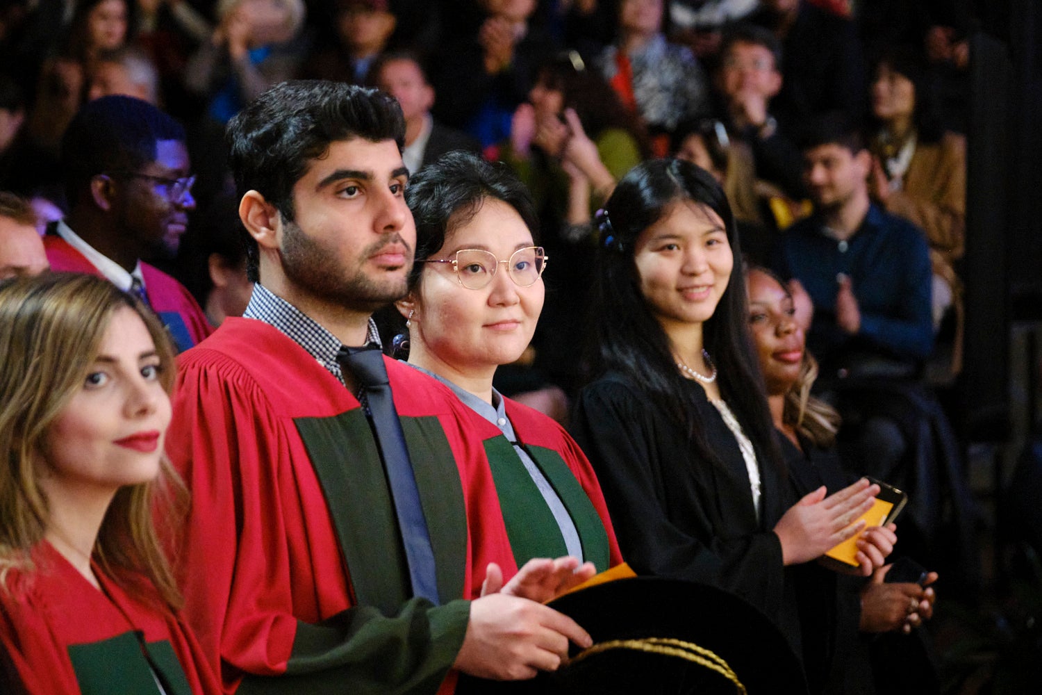Four graduates are seated and smiling while looking at the stage