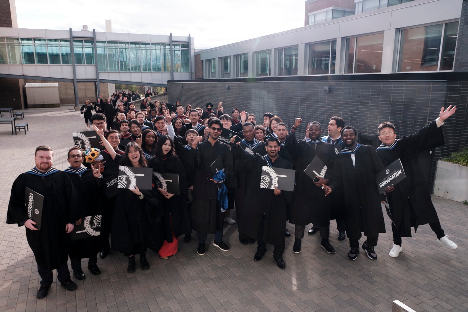 A group of young people in convocation robes pose happily with their degrees