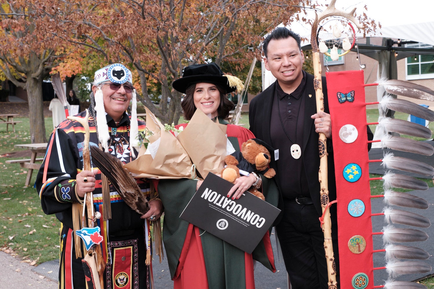 Two men and a woman pose with their Convocation regalia and the woman holds her degree.