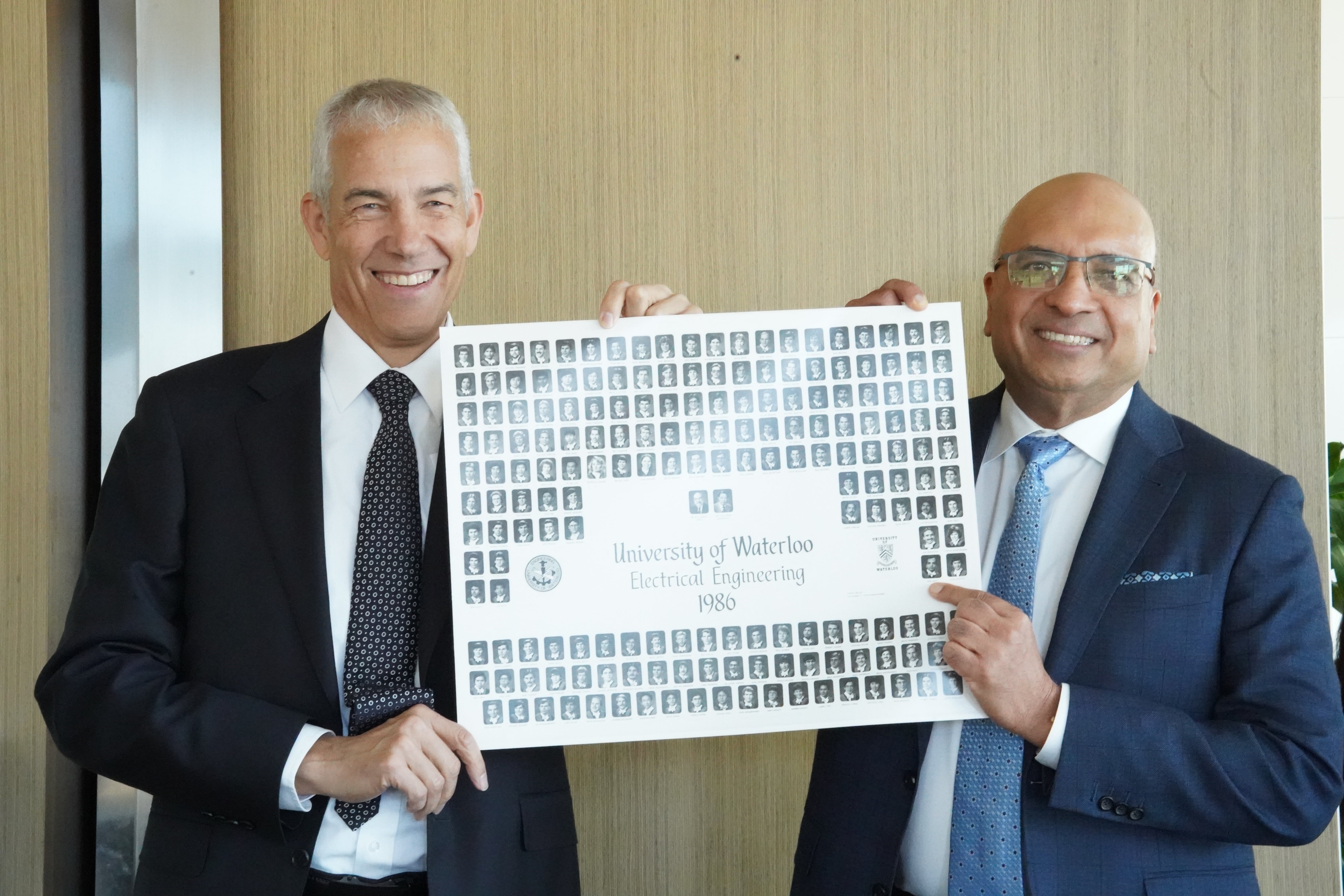 Two men smile and hold a class composite between them